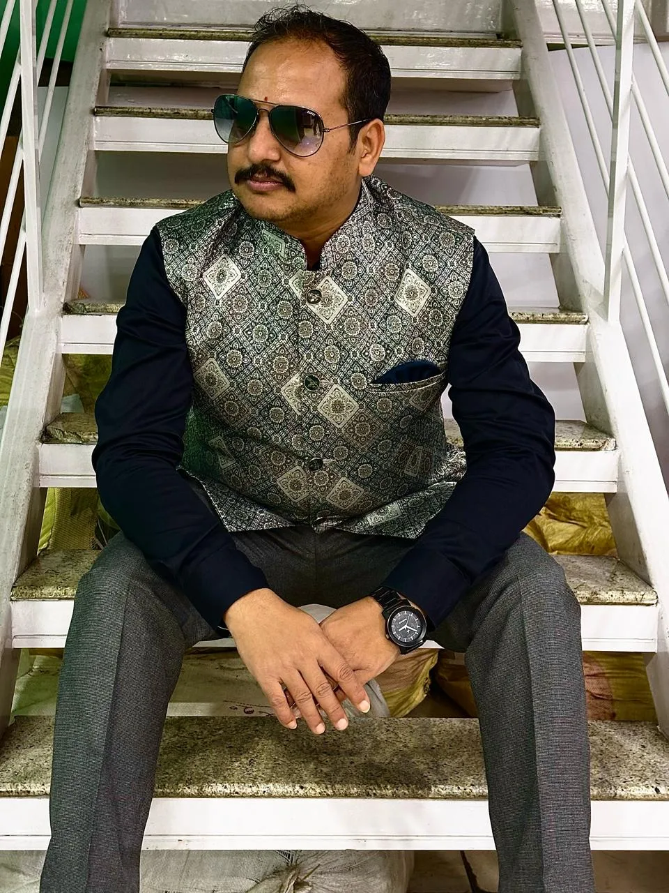 Customer in a printed green-and-cream Nehru jacket over a dark shirt, seated on a staircase