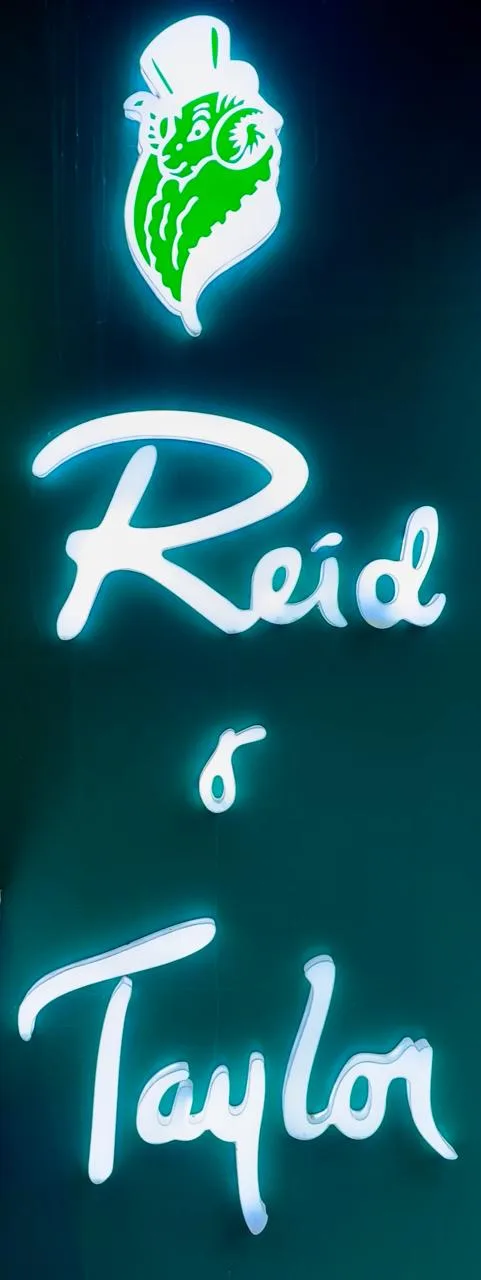 The illuminated Reid & Taylor script sign with the green crowned-ram logo at the Basaveshwaranagar showroom