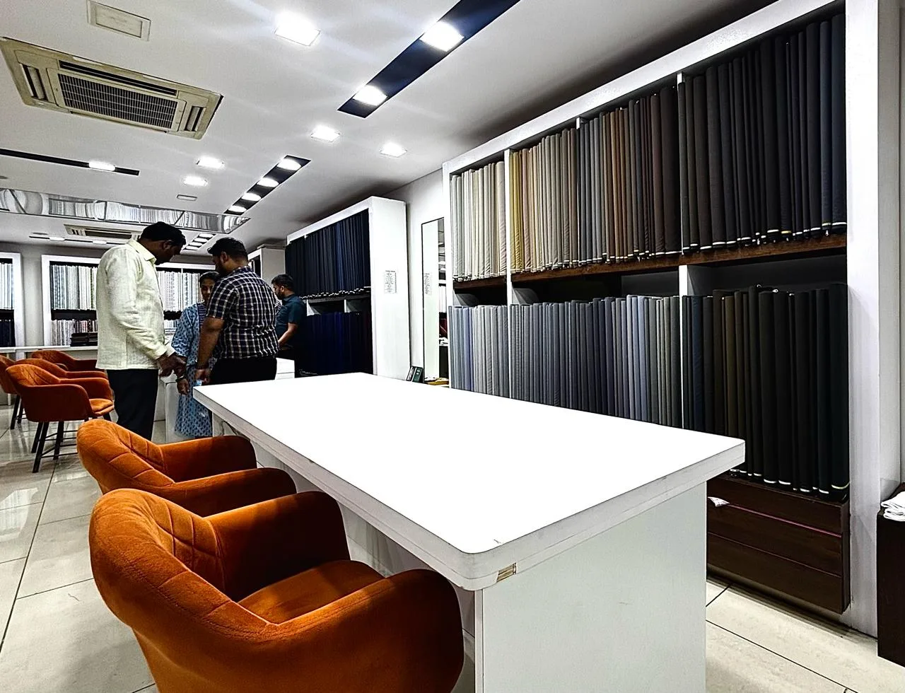 A consultant assisting a customer at the long white consultation table in the Bespoke Studio showroom, with suiting rolls along the wall